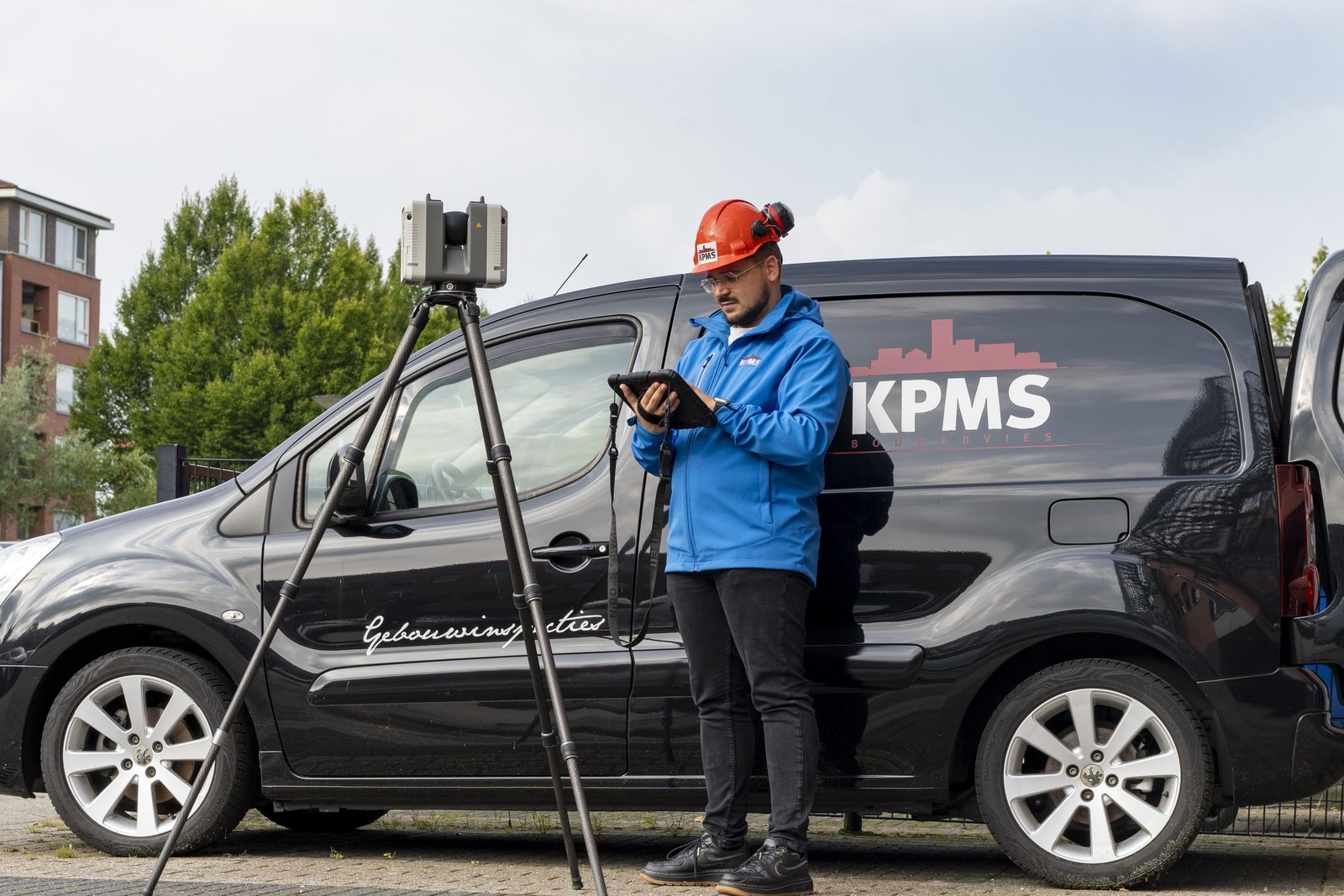 Bouwexpert van KPMS scant een gebouw met een 3D-scanner naast de bus van KPMS