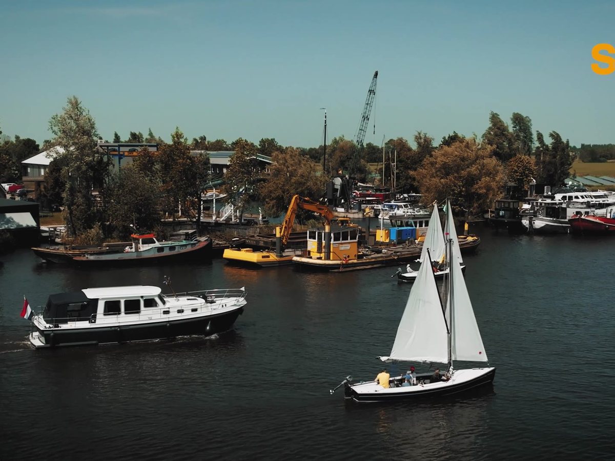 Still uit de commercial: een haven met boten en drijvend materieel